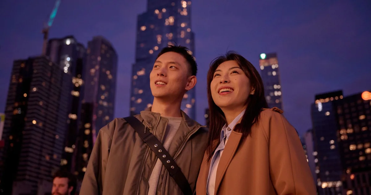 International couple in Queen Victoria Market with skyline behind them.